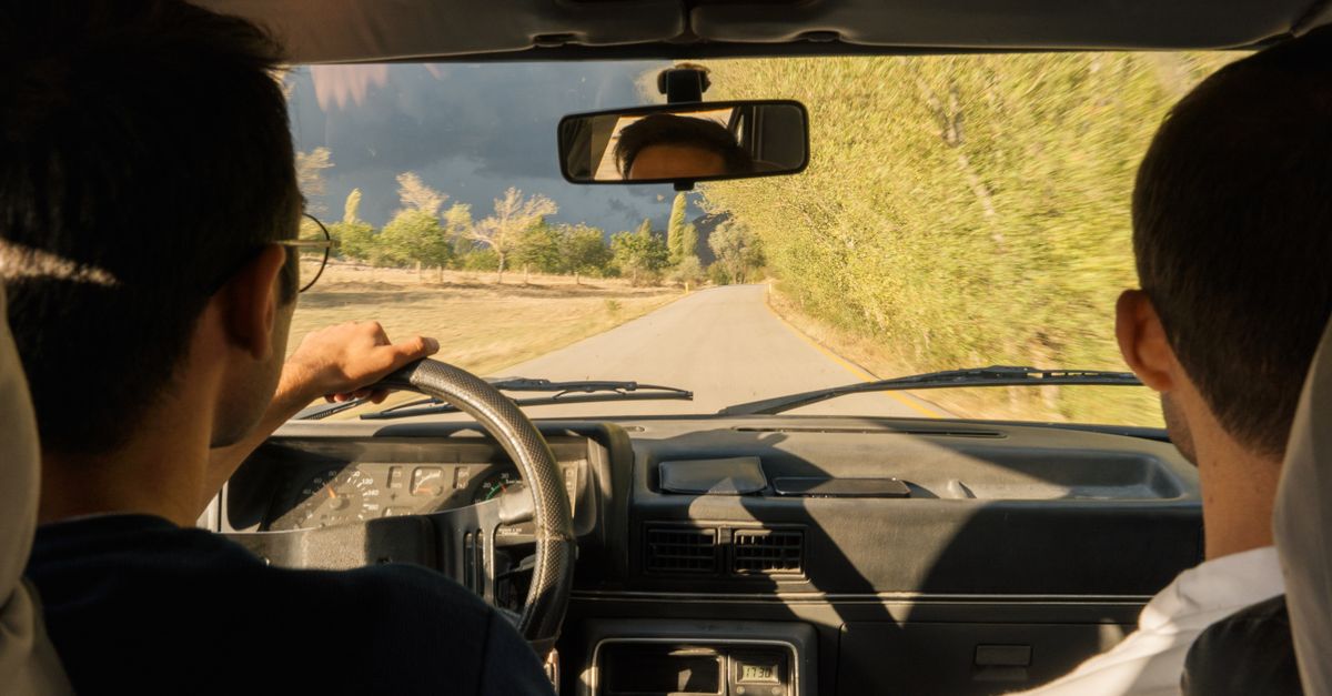Two adults driving through scenic countryside near Merzifon, Türkiye, in a vintage car.