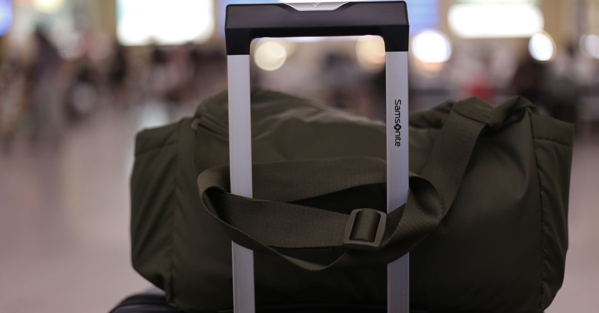 A close-up of a suitcase with a duffel bag on top, in a bustling airport environment.