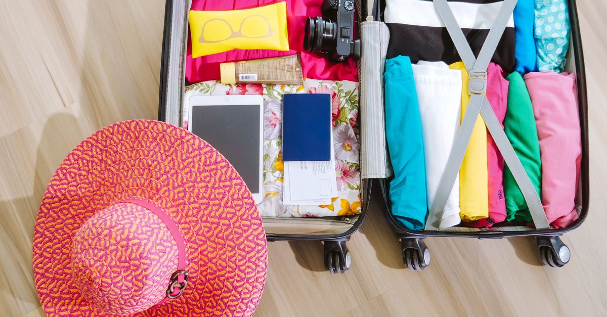 Top view of a suitcase packed with clothes, a camera, and a sun hat, ready for summer travel.
